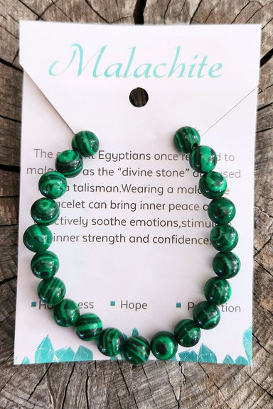Green beaded bracelet on a card with text about malachite on a wooden surface