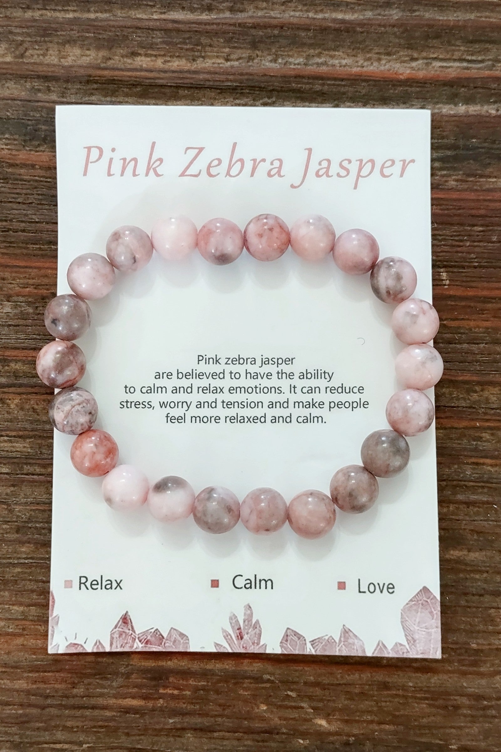 Pink Zebra Jasper bracelet on a card with descriptive text on a wooden surface