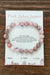Pink Zebra Jasper bracelet on a card with descriptive text on a wooden surface