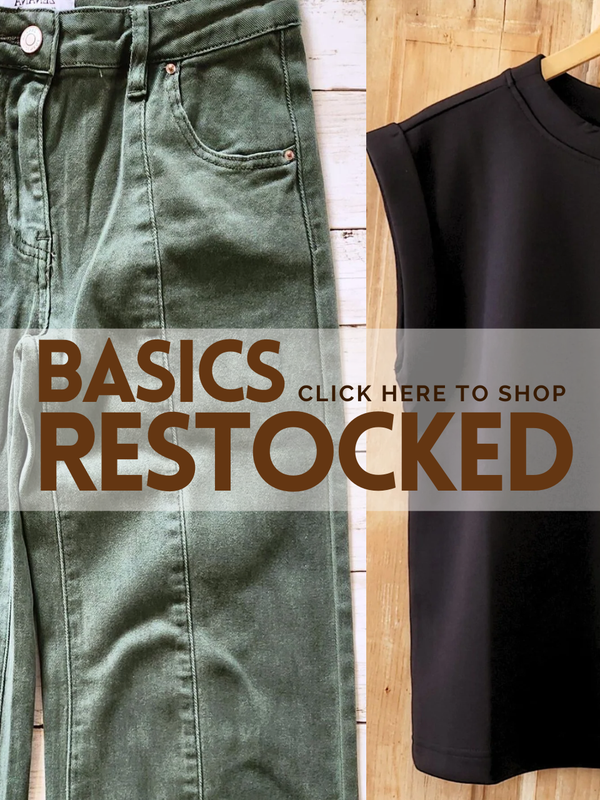 Green jeans and black top on a wooden surface with 'Basics Restocked' text overlay.