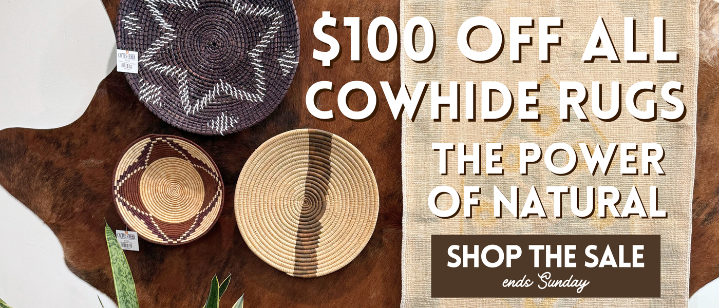 Cowhide rugs with promotional text for a sale on a wooden surface